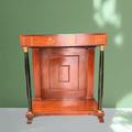 Mueble auxiliar de estilo Imperio con estructura de caoba y frente decorado.