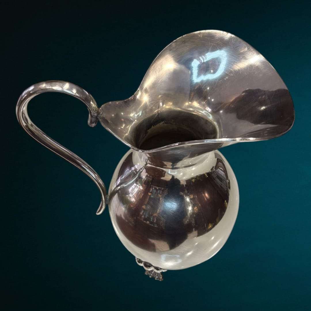 Esta Jarra de metal plateado destaca por su estructura sólida y su exquisita elaboración artesanal, con un diseño cuidado que combina funcionalidad y belleza.