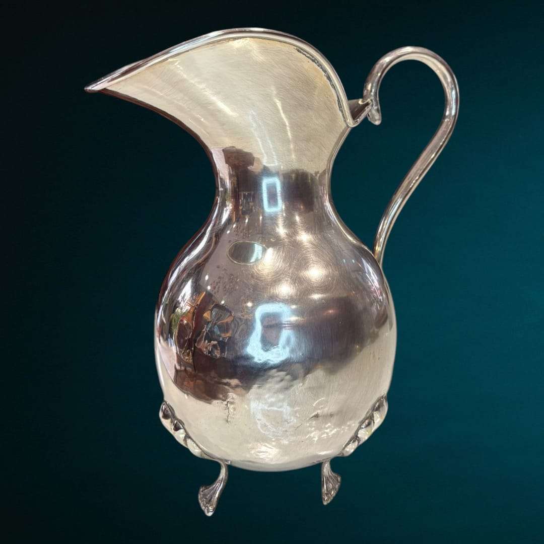 Esta Jarra de metal plateado destaca por su estructura sólida y su exquisita elaboración artesanal, con un diseño cuidado que combina funcionalidad y belleza.