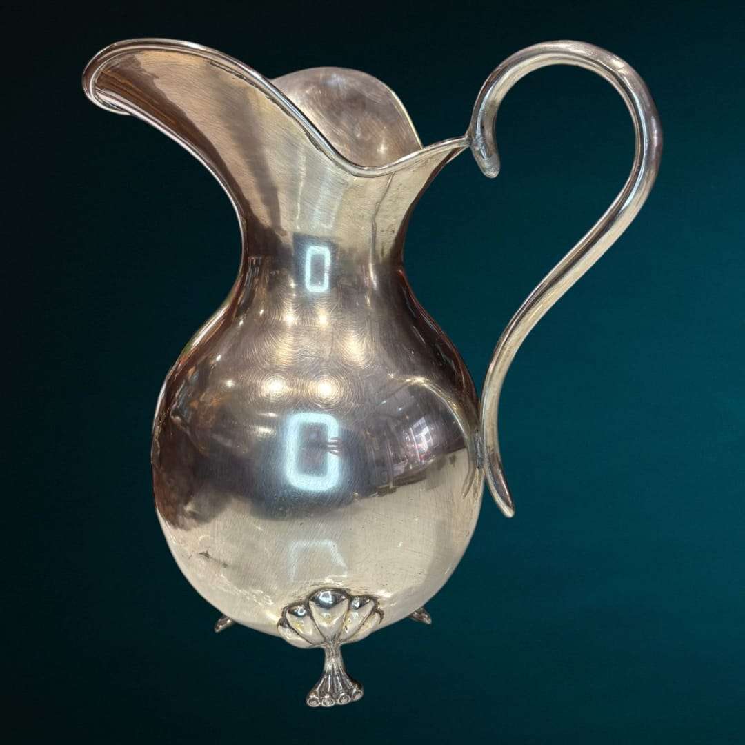 Esta Jarra de metal plateado destaca por su estructura sólida y su exquisita elaboración artesanal, con un diseño cuidado que combina funcionalidad y belleza.