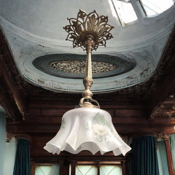 Lámpara de techo vintage con tulipa pintada a mano, instalada en techo decorado con molduras clásicas. Ideal para decoración elegante de interiores.