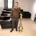 Lampara India antigua de metal y cobre artesanal única junto a una persona para mostrar su gran altura. Decoración oriental exclusiva para el hogar.