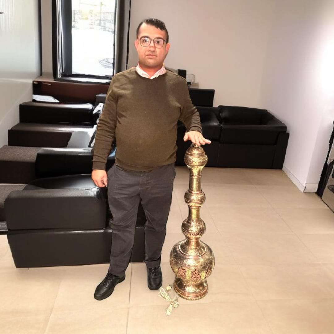 Lampara India antigua de metal y cobre artesanal única junto a una persona para mostrar su gran altura. Decoración oriental exclusiva para el hogar.