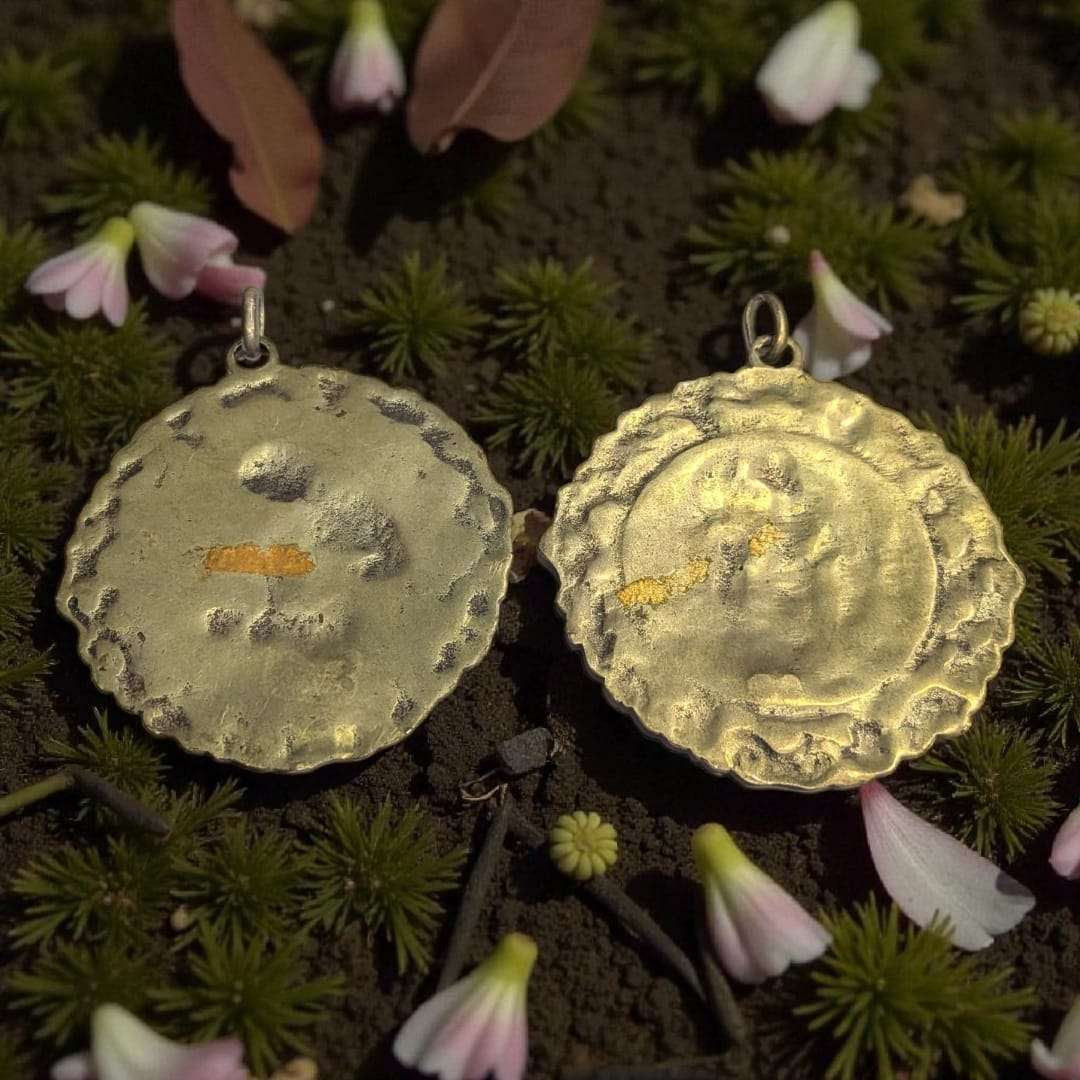 Medallas de metal fundido con relieves religiosos únicos, Virgen con Niño Jesús y Ángel de la Guarda con niña, sobre fondo decorado con flores rosadas.