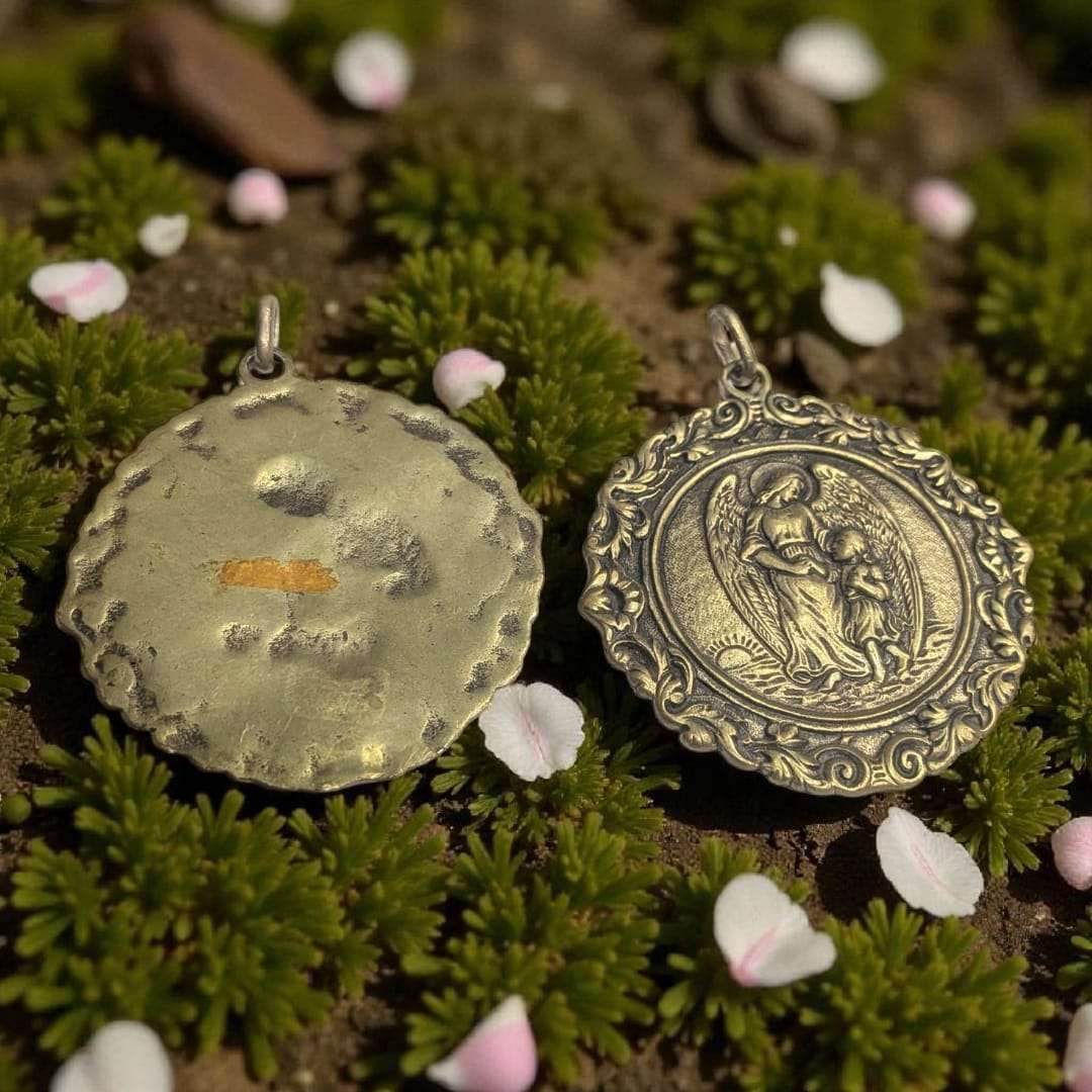 Medalla de metal fundido con relieve religioso del Ángel de la Guarda con niña, diseño artesanal sobre fondo natural con pétalos y musgo.