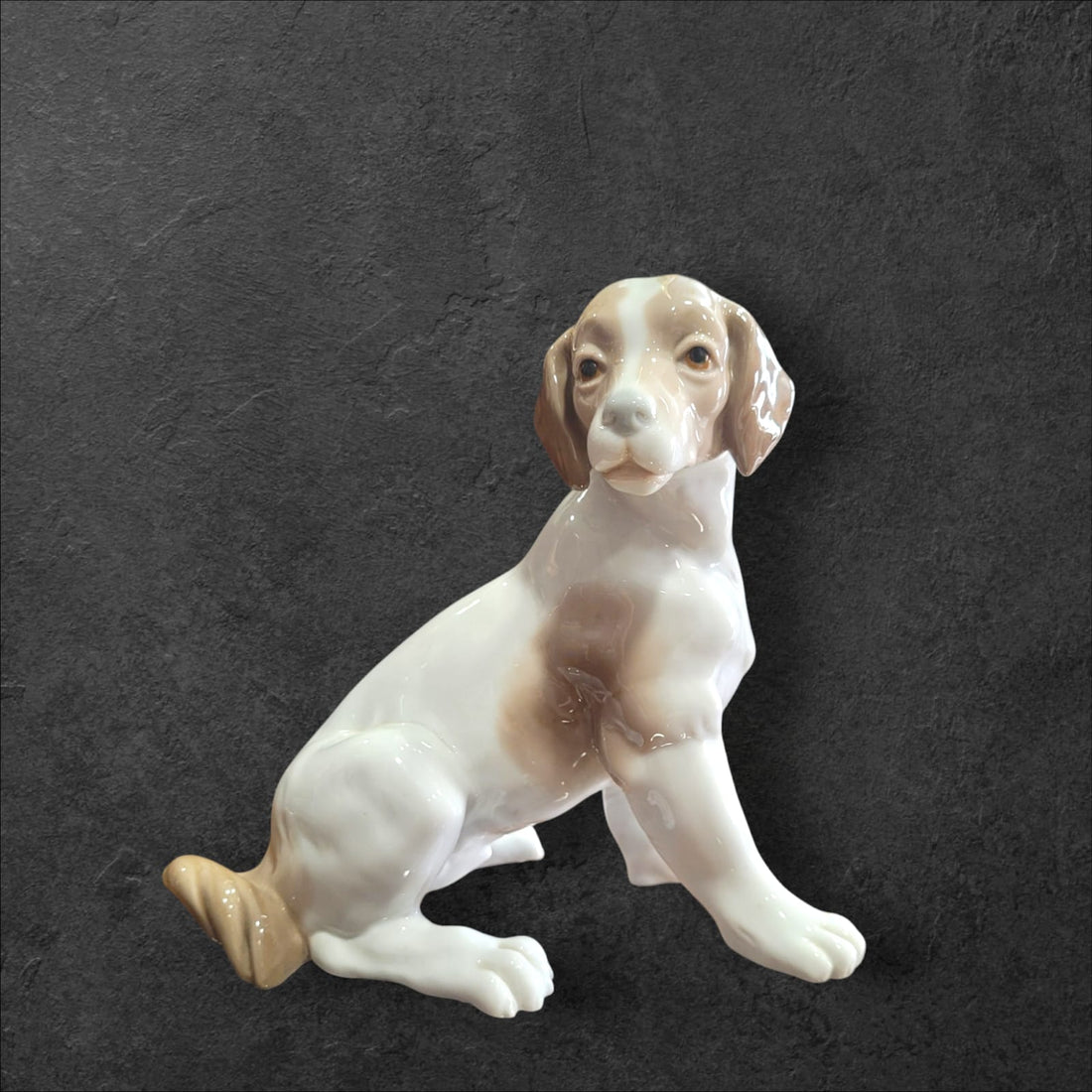 Figura de perro manchado en porcelana fina Nao Lladró, diseño bicolor con orejas caídas, ideal para decoración elegante en el hogar.