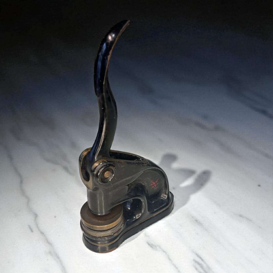 Sello de relieve antiguo de metal negro visto en perspectiva lateral.