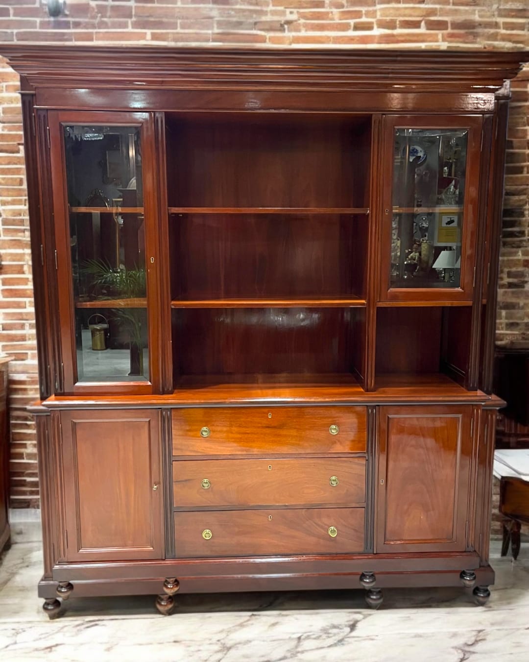 Librería-aparador de caoba maciza con detalles clásicos, ideal para organizar y decorar. Diseño elegante con vitrinas de vidrio y cajones espaciosos.