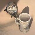 Jarra de cerveza alemana de porcelana con tapa metal abierta, decorada con escudo y texto en latín. Ideal para decoración vintage en el hogar.
