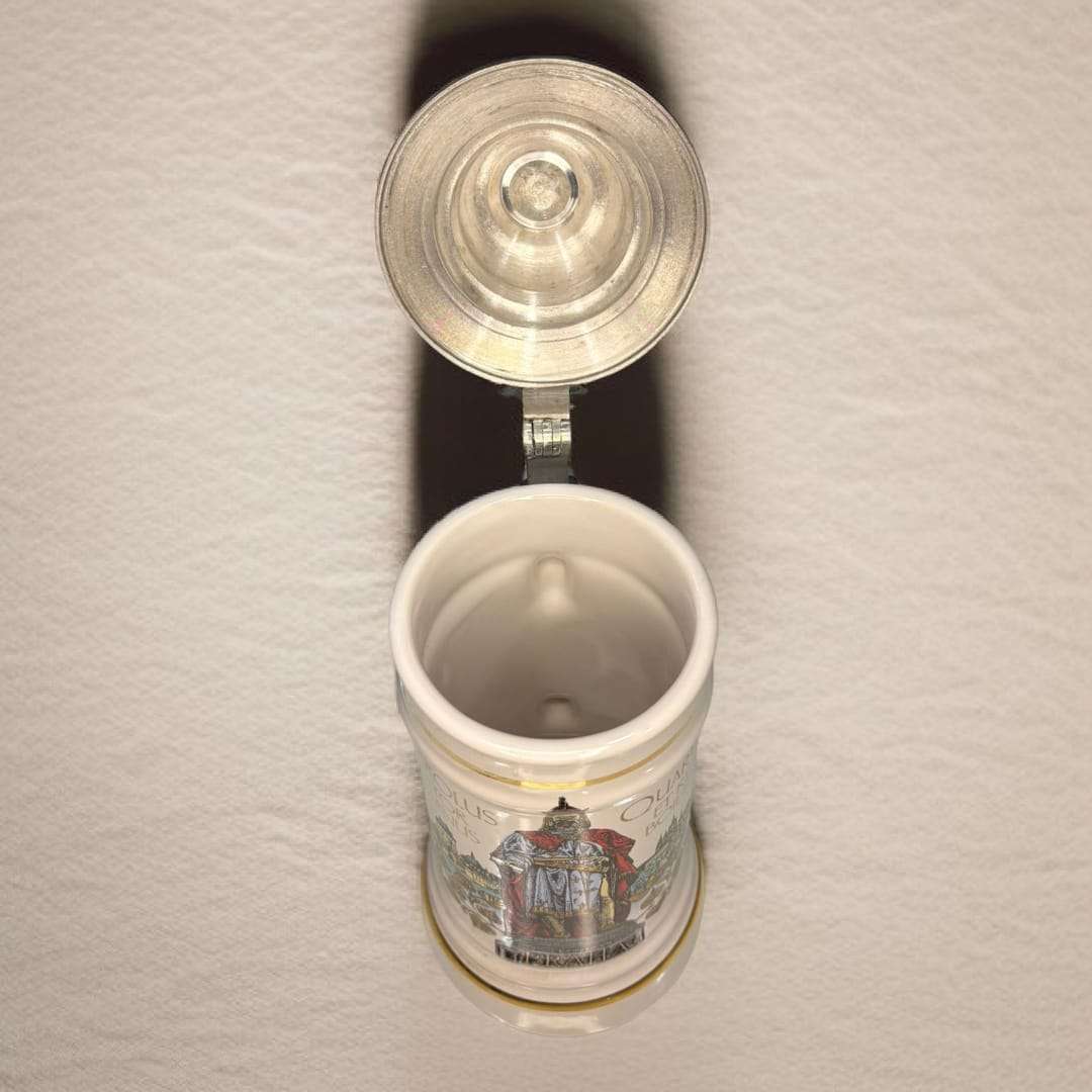 Jarra de cerveza alemana de porcelana con tapa metal abierta, decorada con ilustraciones históricas y texto en latín. Ideal para decoración vintage.