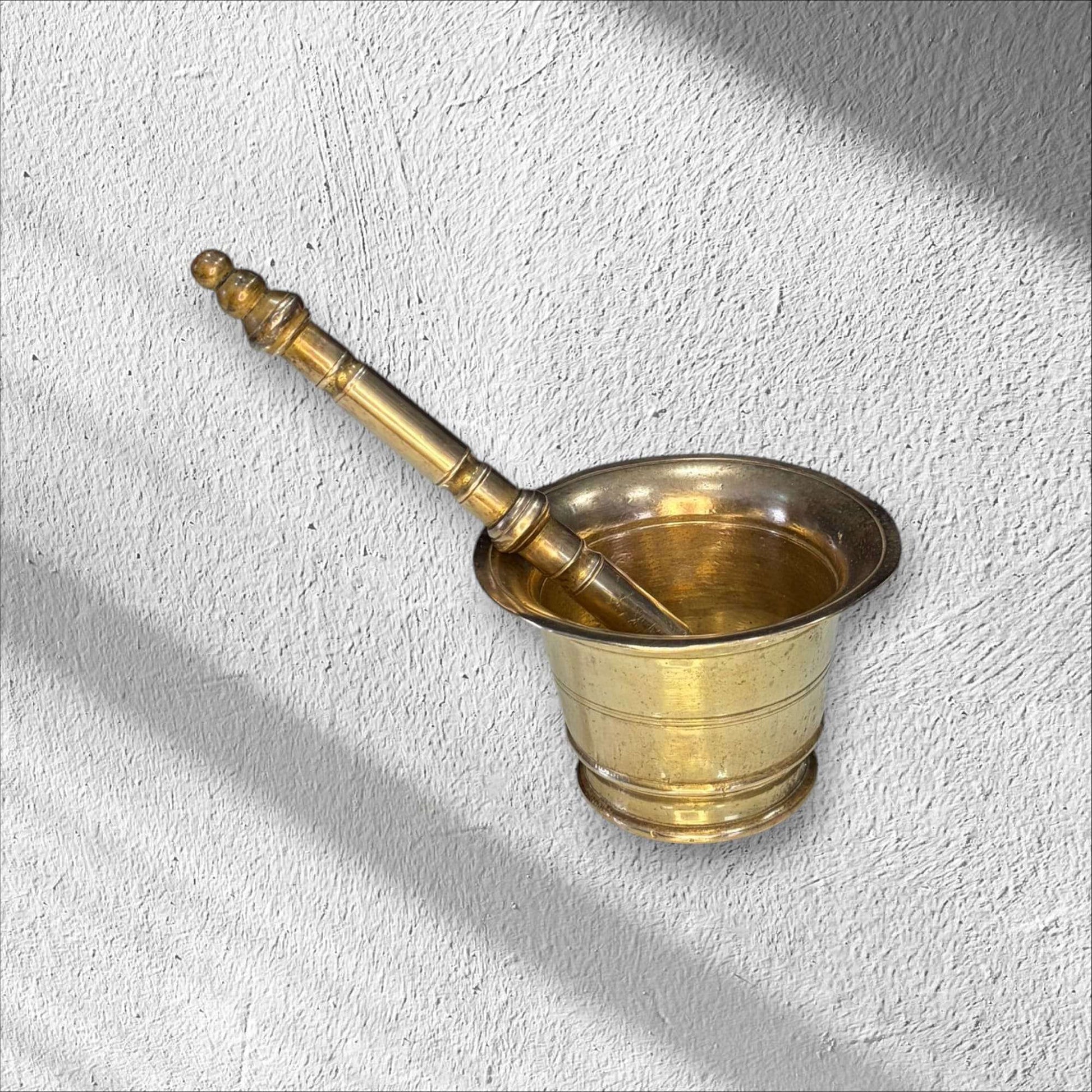 Mortero de bronce antiguo con maja colocada dentro, diseño robusto y elegante, ideal para ambientaciones de estilo histórico o rural.