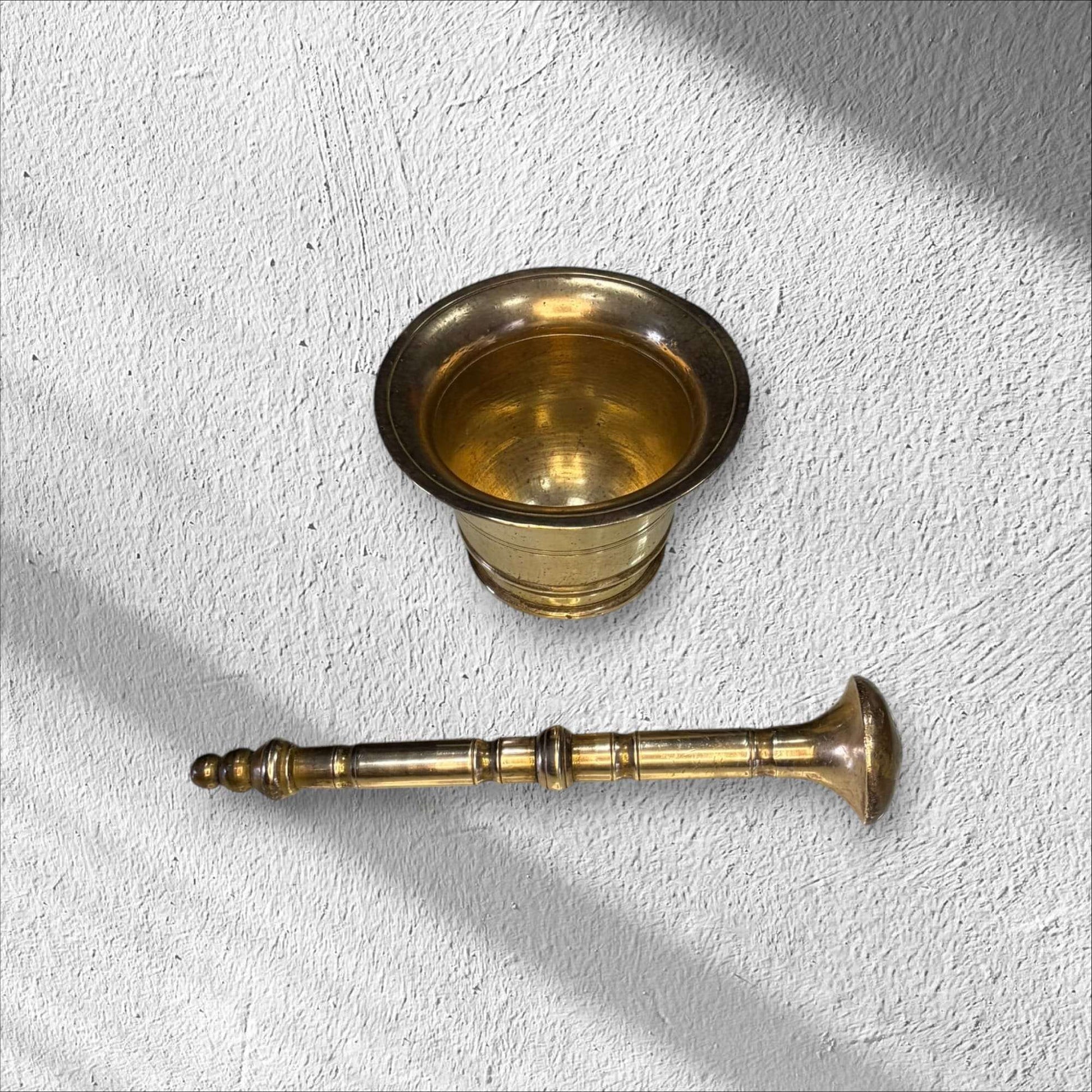 Mortero de bronce antiguo con la maja separada, mostrando su diseño completo, pieza auténtica para decoración de cocina o jardín.