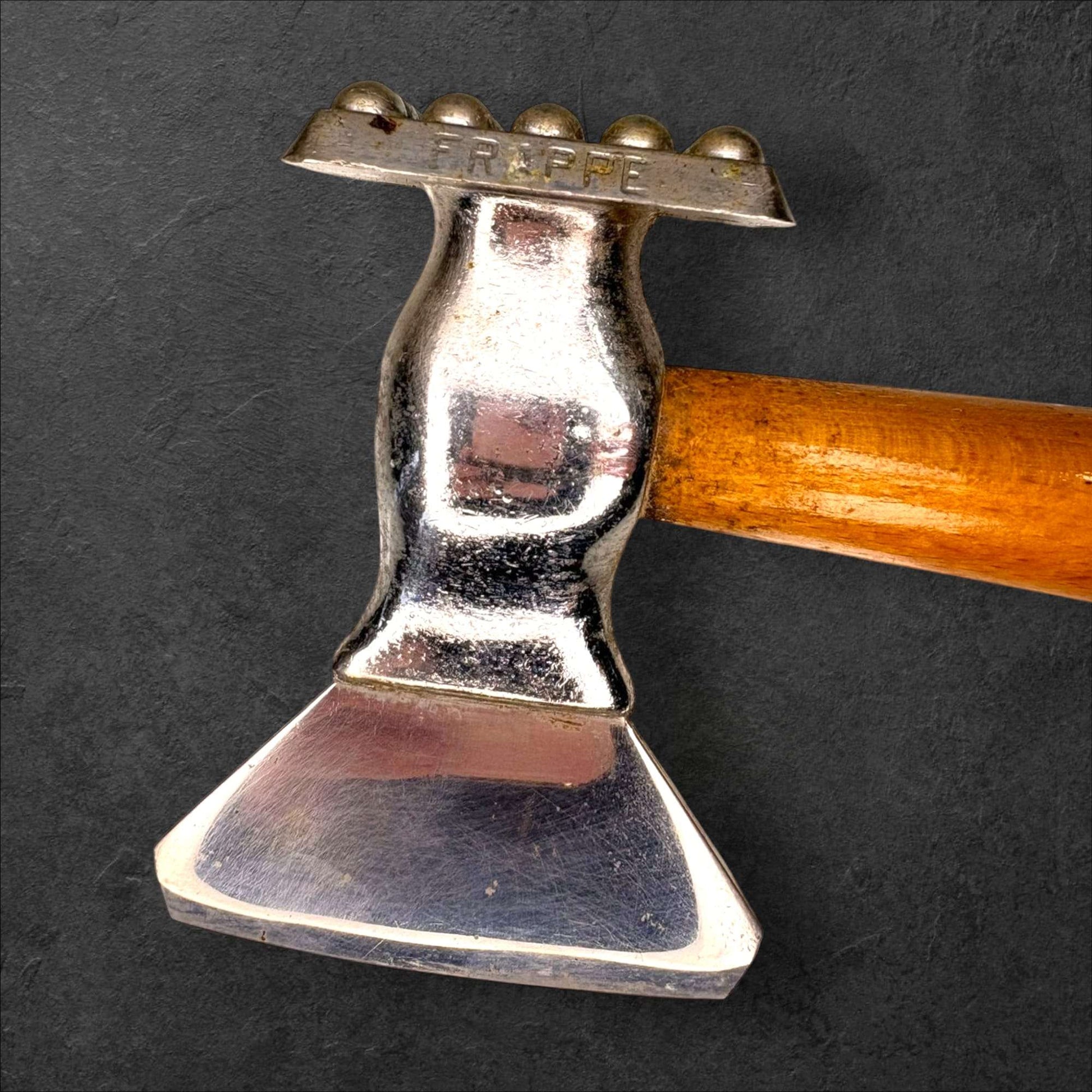Primer plano del cabezal de acero del martillo y hachuela con inscripción 'FRAPPE', herramienta decorativa de carnicería antigua para colección.