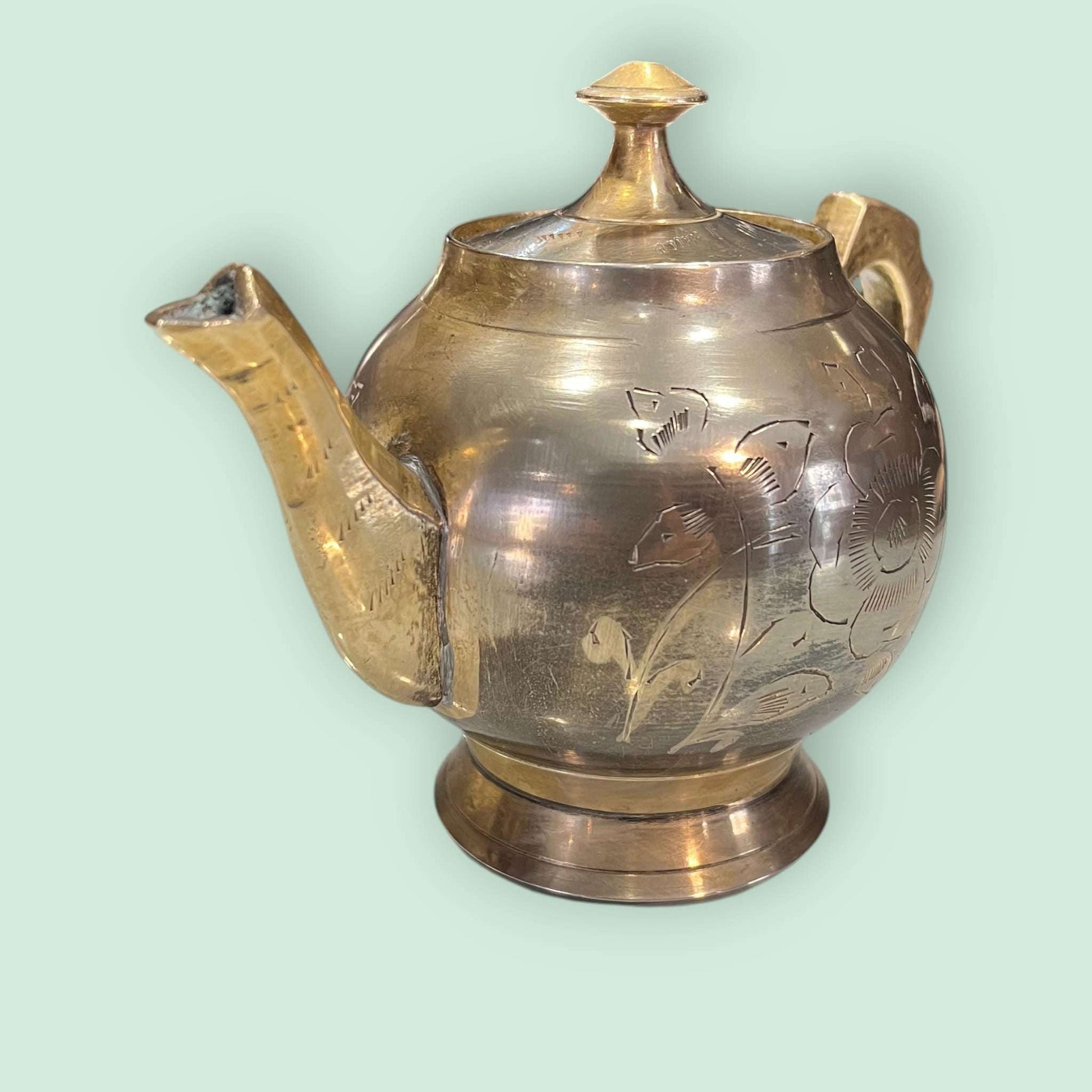 Tetera de metal dorado antigua con pico curvo y grabados florales, ideal para decoración elegante en espacios vintage o rústicos.