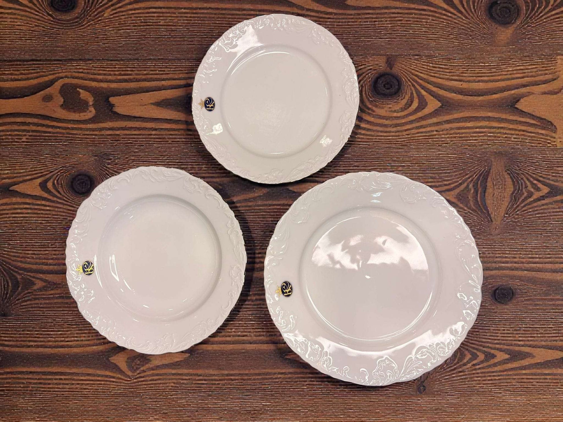 Tres platos de porcelana Royal George V con relieves y filo dorado sobre mesa de madera, ideales para mesa de gala o colección decorativa.