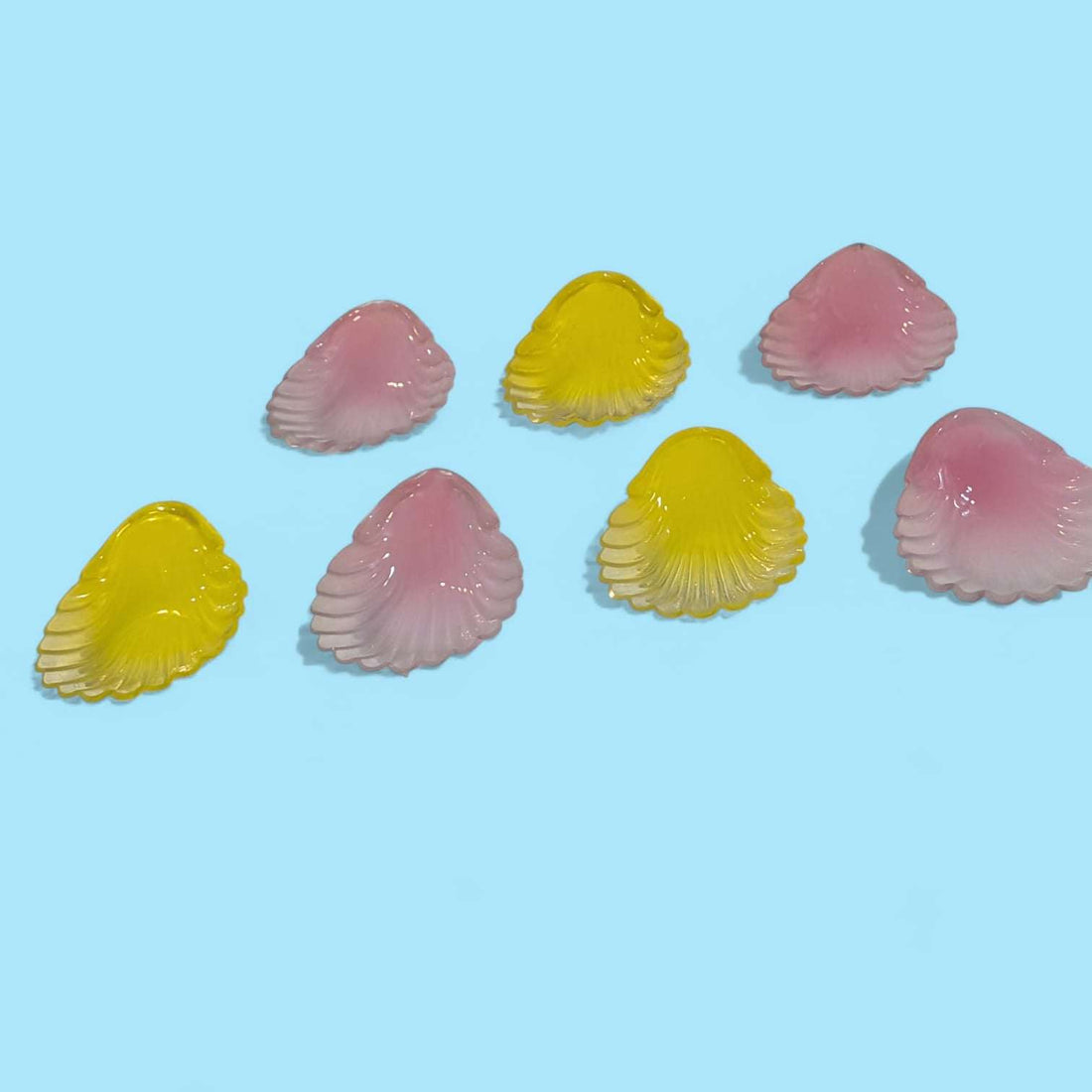 Conjunto de conchas de cristal de colores rosa y amarillo antiguas sobre fondo azul, ideales para decoración vintage y coleccionismo exclusivo.