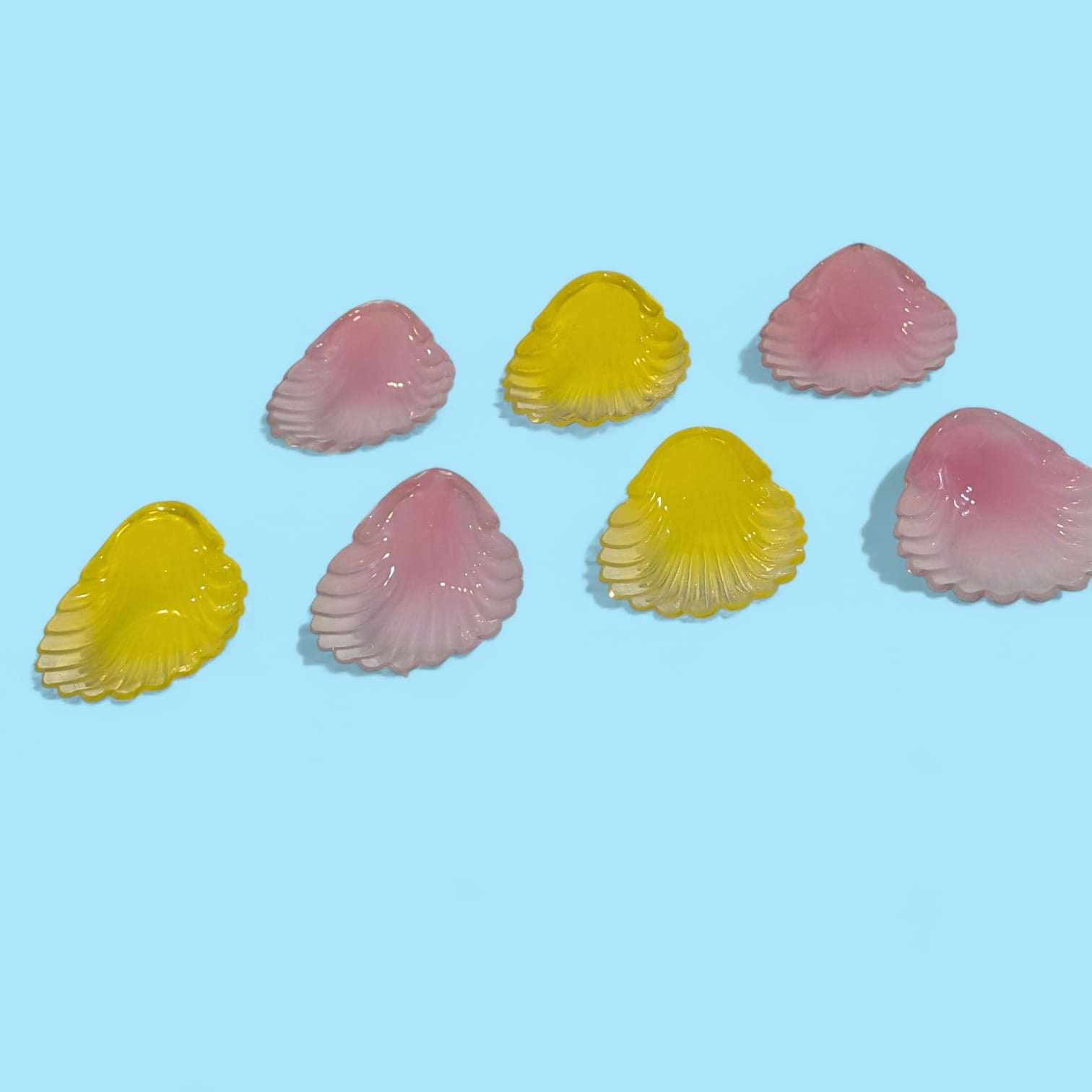 Conjunto de conchas de cristal de colores rosa y amarillo antiguas sobre fondo azul, ideales para decoración vintage y coleccionismo exclusivo.