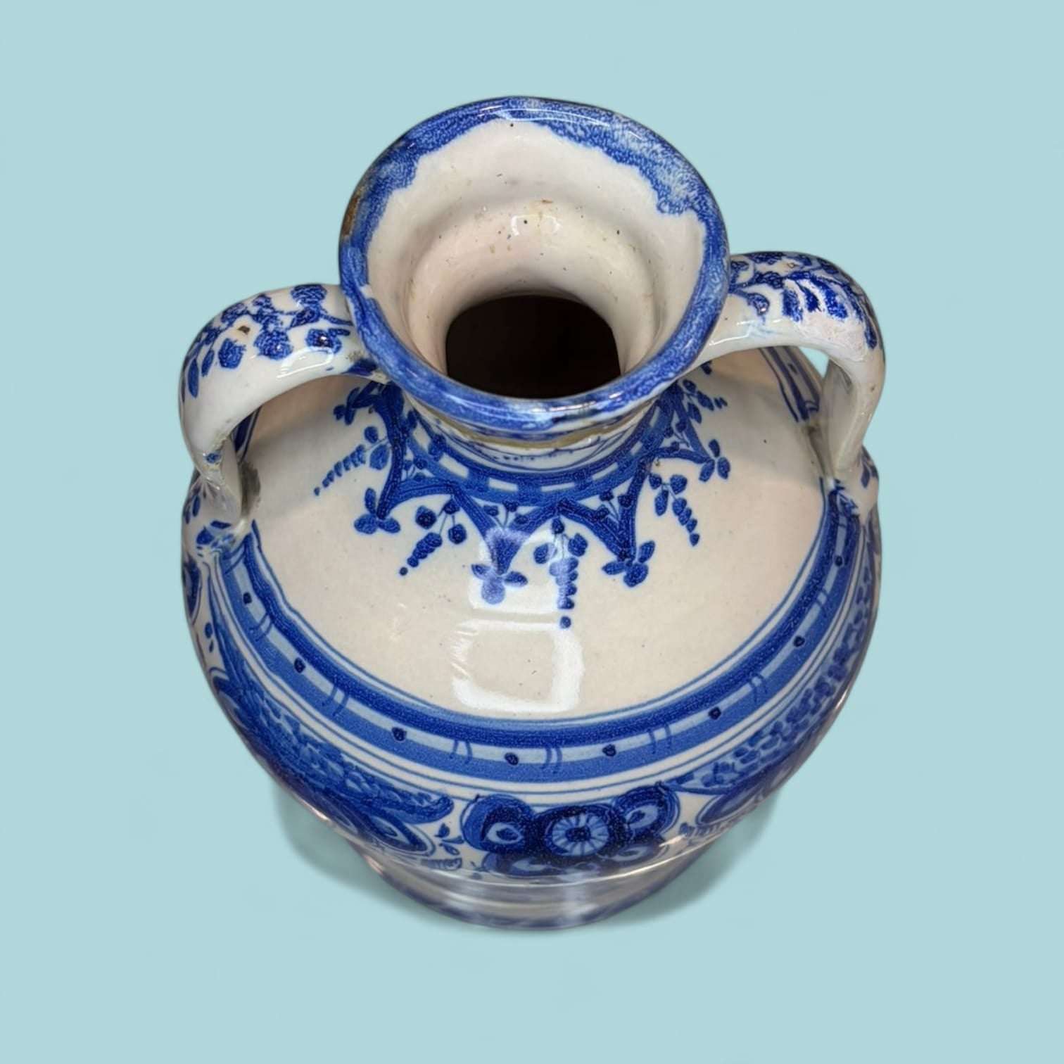 Vista superior de ánfora de cerámica esmaltada azul con borde decorado y asas ornamentadas. Pieza única para decoración de hogar o jardín.