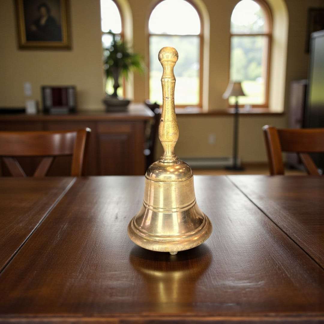 Campana de metal dorado antigua sobre mesa de madera en sala clásica. Decoración elegante para escritorio o recibidor con sonido noble.