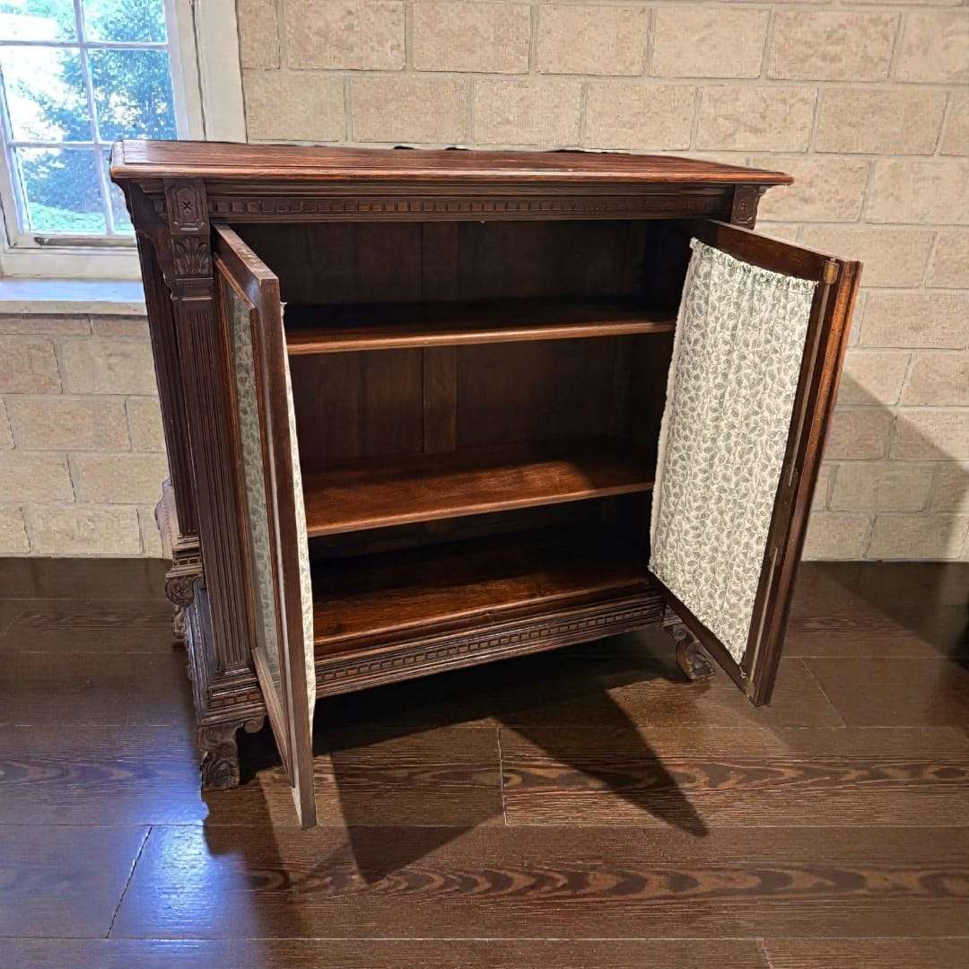 Interior de vitrina de madera clásica con dos puertas abiertas y estantes amplios. Cortinas decorativas en las puertas para proteger objetos.