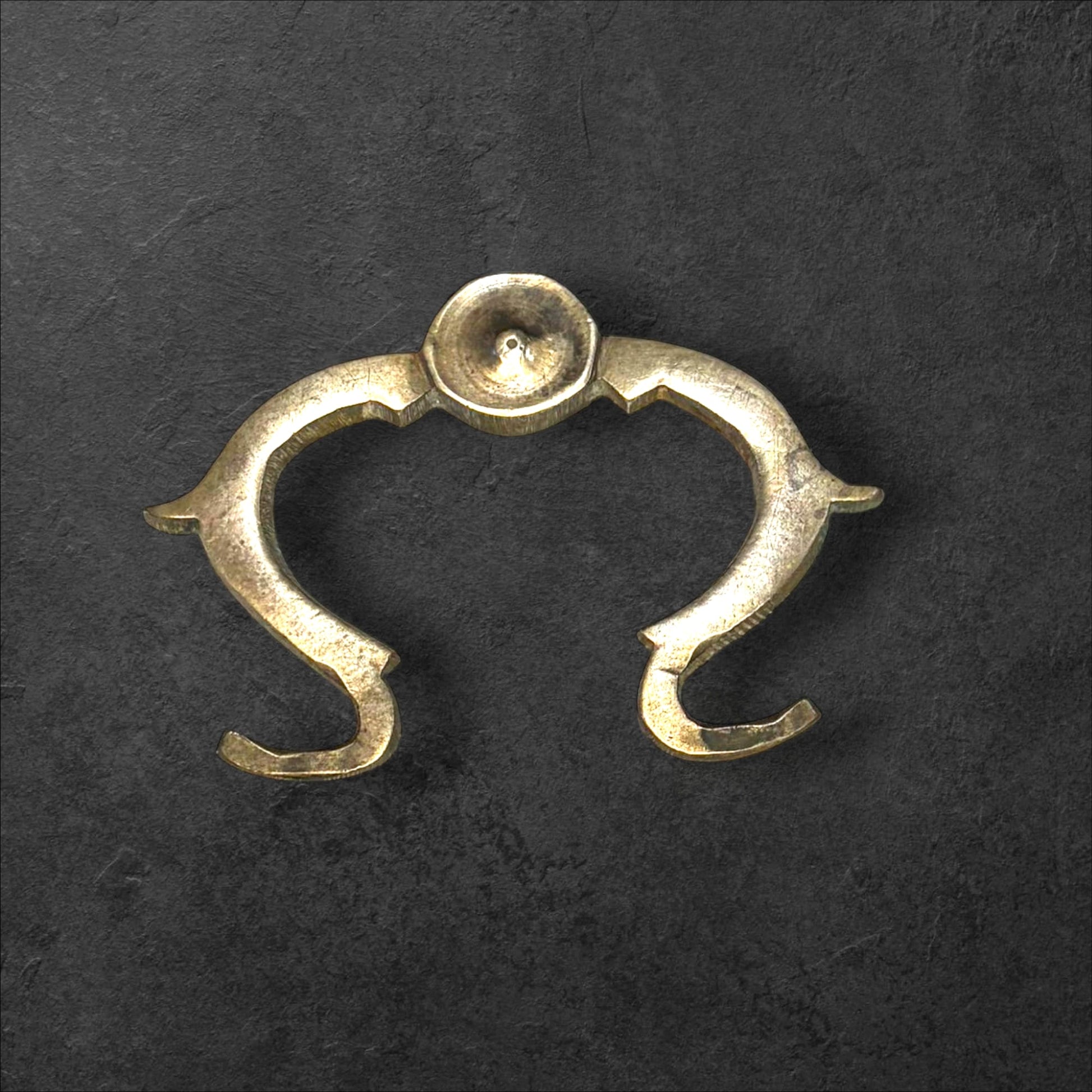 Tirador de metal antiguo original para muebles único con diseño curvo y acabado envejecido sobre fondo oscuro. Ideal para decoración vintage.