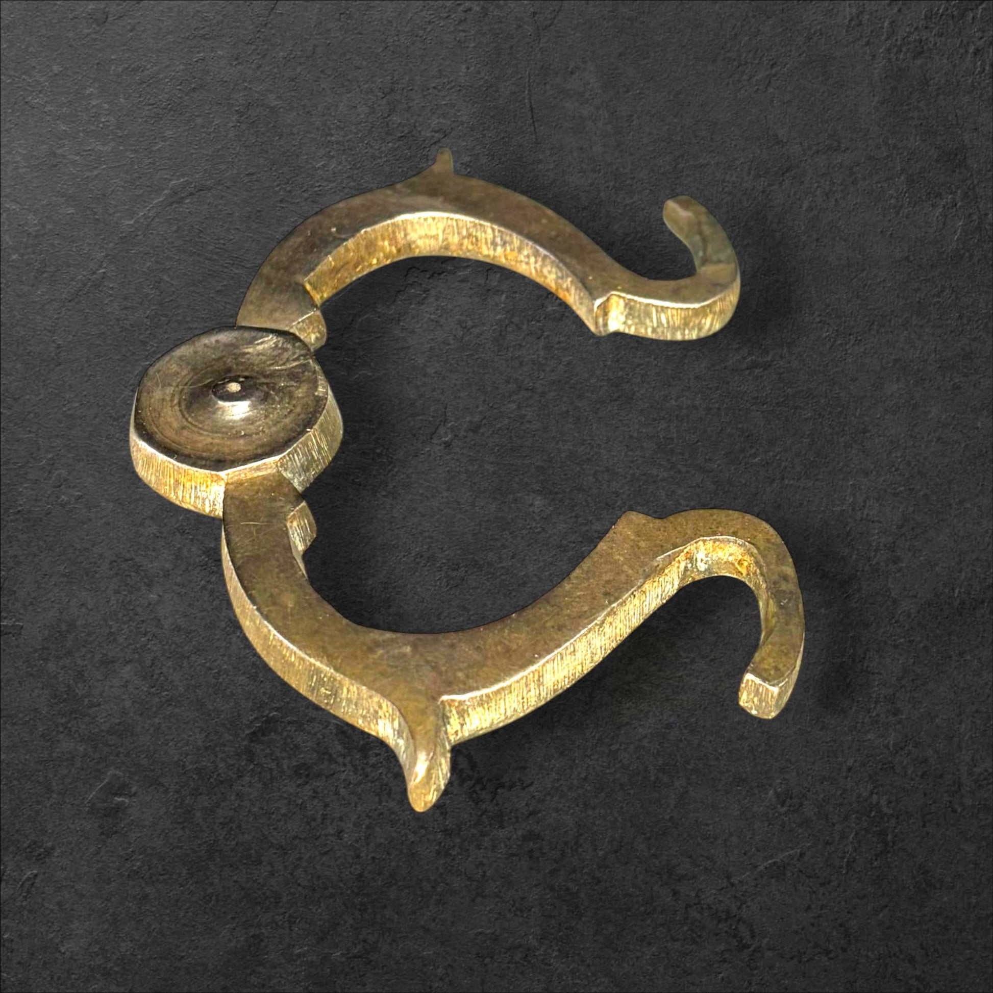 Tirador de metal antiguo original para muebles único con diseño curvo y acabado envejecido sobre fondo oscuro. Ideal para decoración vintage.