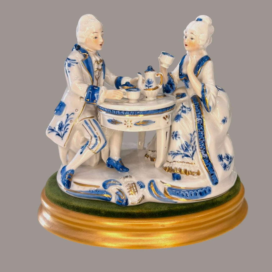 Figura de porcelana continental vintage azul y blanco con pareja rococó tomando té en mesa redonda, decorada con detalles dorados y base dorada.
