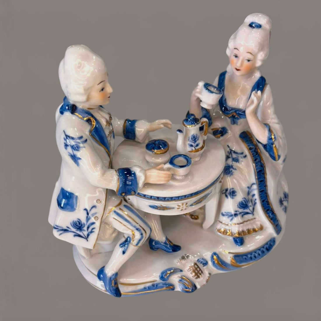 Figura de porcelana continental vintage azul y blanco con pareja rococó tomando té en mesa redonda, decorada con detalles dorados y base dorada.