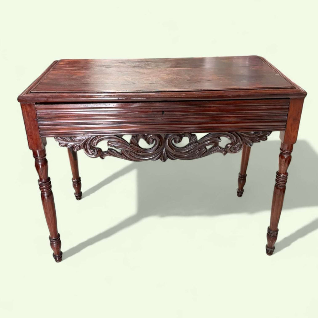 Mesa consola de caoba tallada antigua con cajón única, con detalles ornamentales en el faldón y patas torneadas, ideal para decoración clásica.