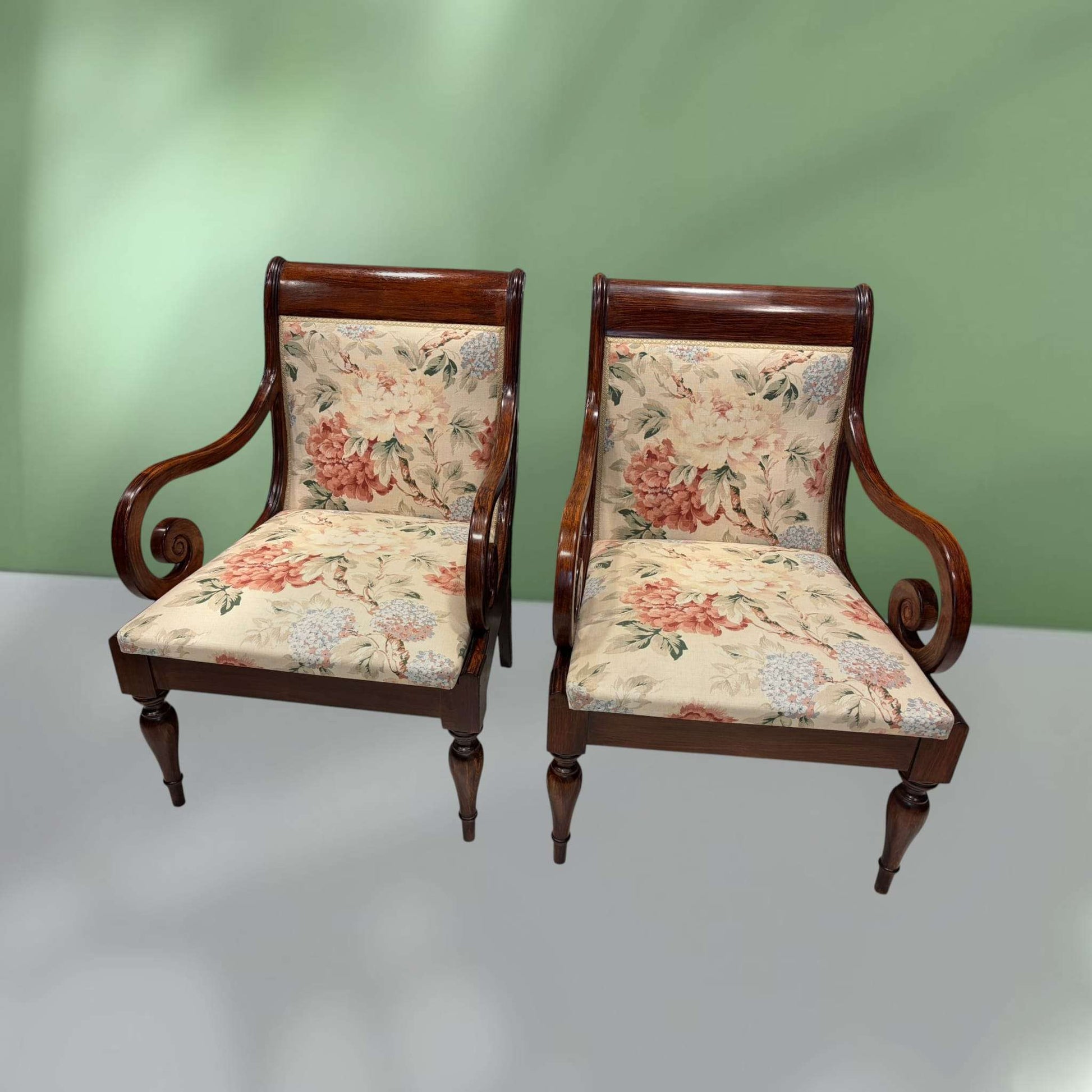 Conjunto de sillones de madera con brazos curvos y tapizado floral, perfectos para decoración clásica en hogar o jardín interior.