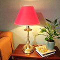 Lámpara sobre mesa metal pantalla burdeo claro 44 cm en mueble de madera junto a planta decorativa. Ideal para lectura o decoración clásica.