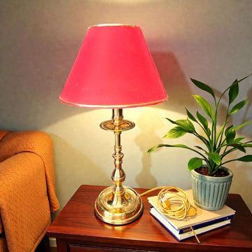 Lámpara sobre mesa metal pantalla burdeo claro 44 cm en mueble de madera junto a planta decorativa. Ideal para lectura o decoración clásica.