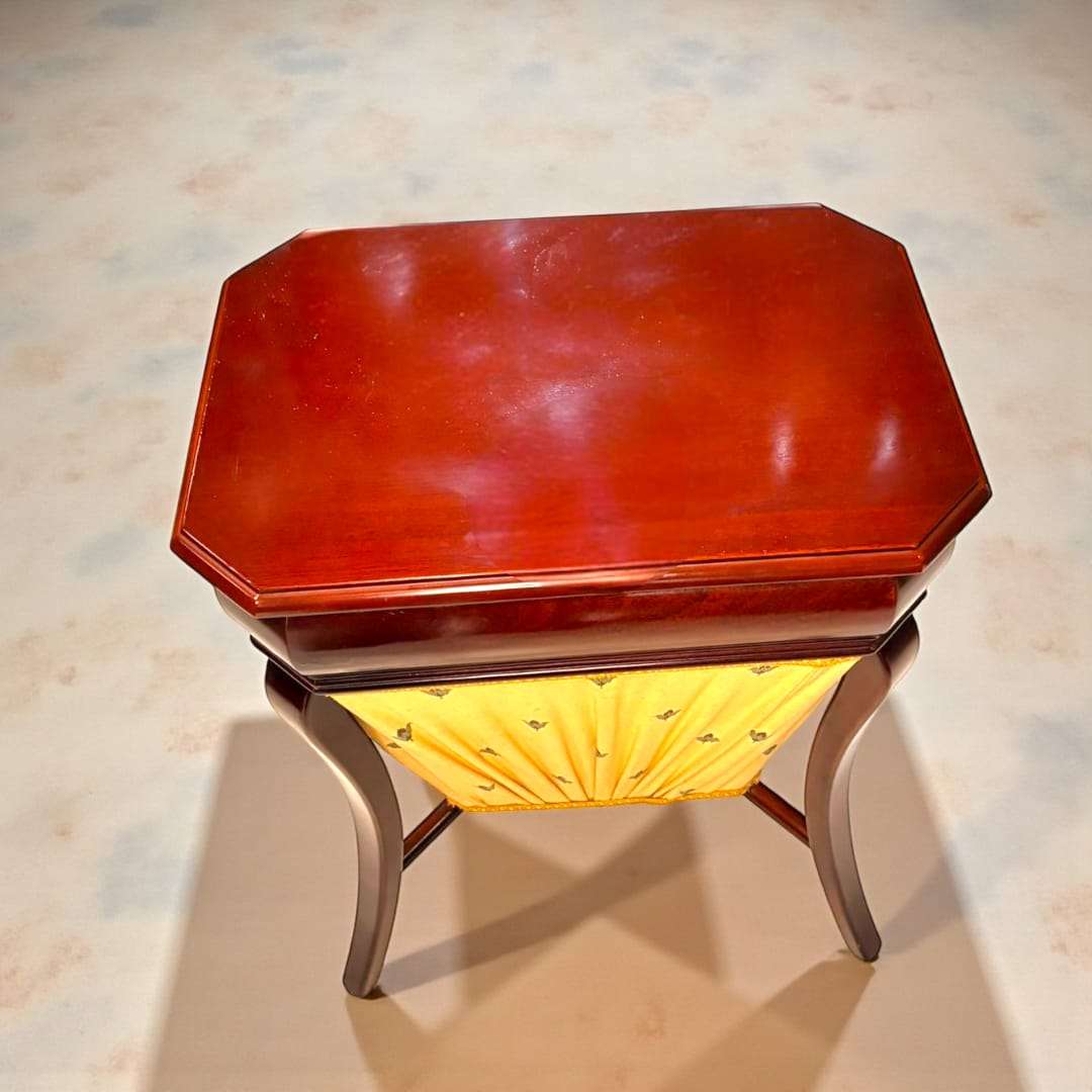 Costurero de caoba clásico con compartimentos, tapa abatible y faldón amarillo decorado. Ideal para decoración vintage en hogar elegante.
