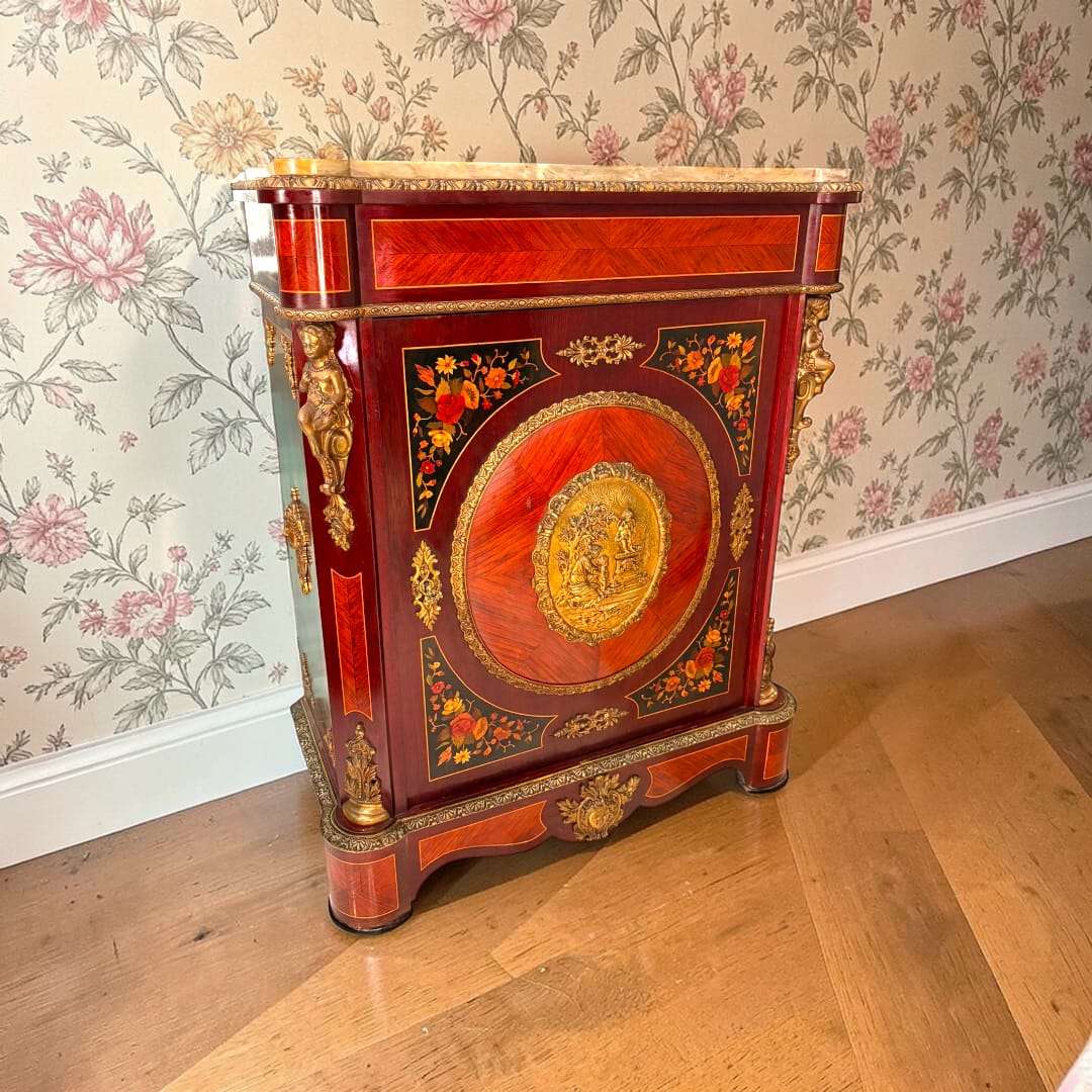  En las imágenes se aprecia una pieza de gran riqueza ornamental, con una composición frontal protagonizada por una gran puerta central decorada, laterales con apliques figurativos y una tapa superior de mármol claro que aporta contraste, luminosidad y nobleza al conjunto. 