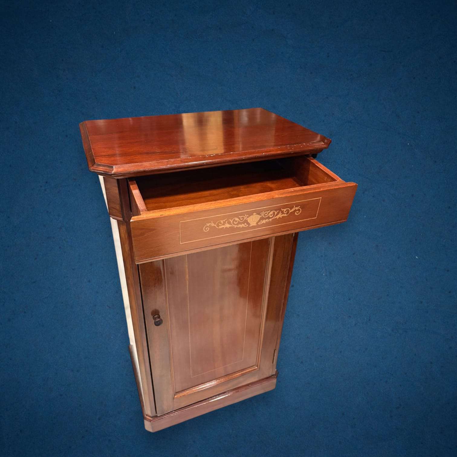 En las imágenes se aprecia una estructura sobria y elegante, con cajón superior, puerta frontal panelada y un frente rematado con taracea lineal y motivo ornamental central en la franja del cajón. 