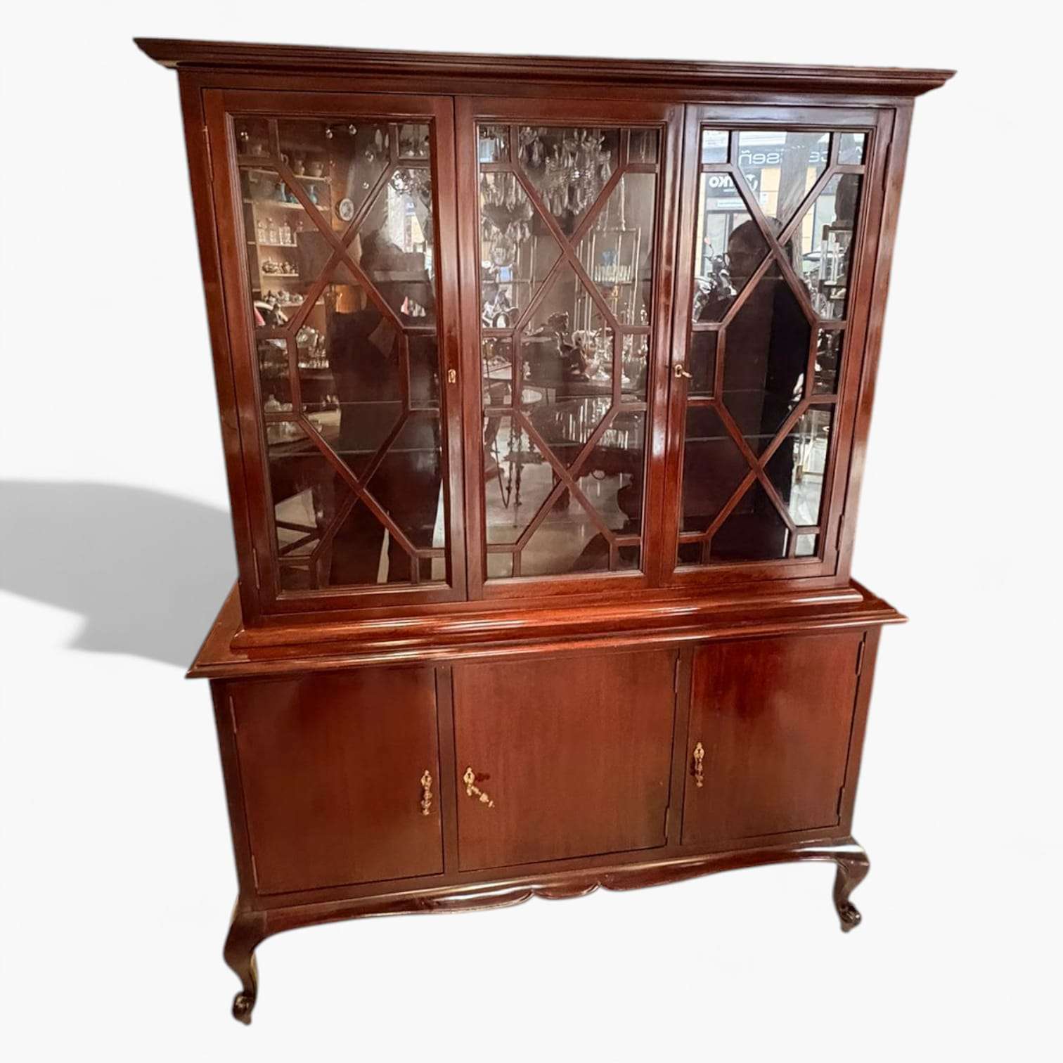 Lo que diferencia a esta pieza es su equilibrio entre sobriedad y detalle. La Vitrina de caoba presenta una estructura de líneas clásicas, con copete superior moldurado de gran vuelo, friso intermedio saliente y una base con patas delanteras curvadas que aligeran visualmente el conjunto. 