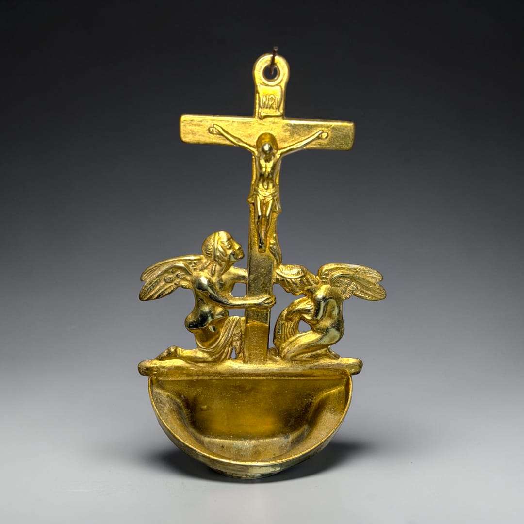 Esta benditera de bronce es una pieza de fuerte valor simbólico y gran presencia visual, concebida originalmente para contener agua bendita y colocarse en la pared de un hogar, capilla o espacio de devoción privada. 