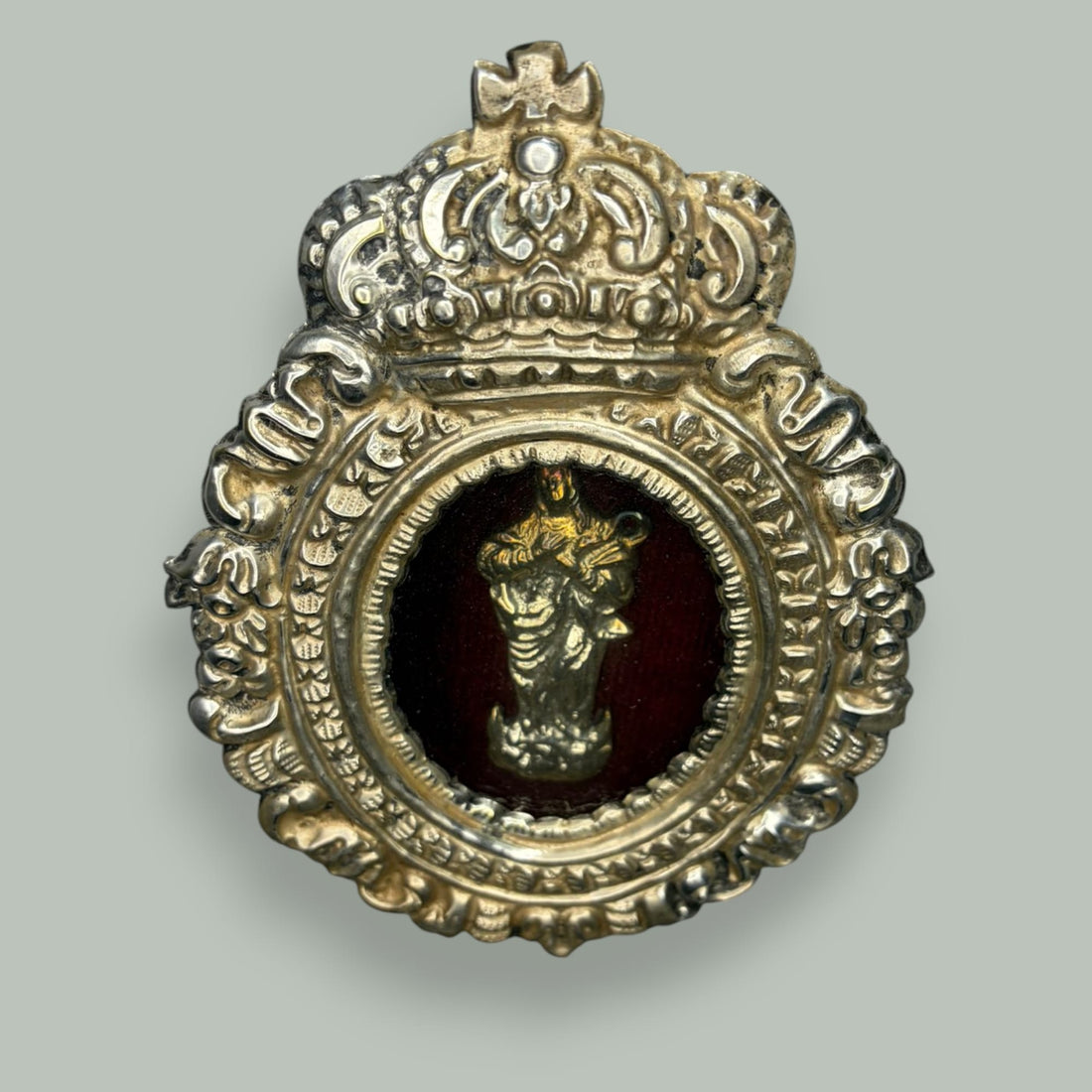 Este relicario de metal plateado con imagen de la Virgen es una pieza devocional de gran encanto, concebida originalmente para custodiar una imagen sagrada en el ámbito doméstico, acompañando la oración privada y la contemplación cotidiana. 