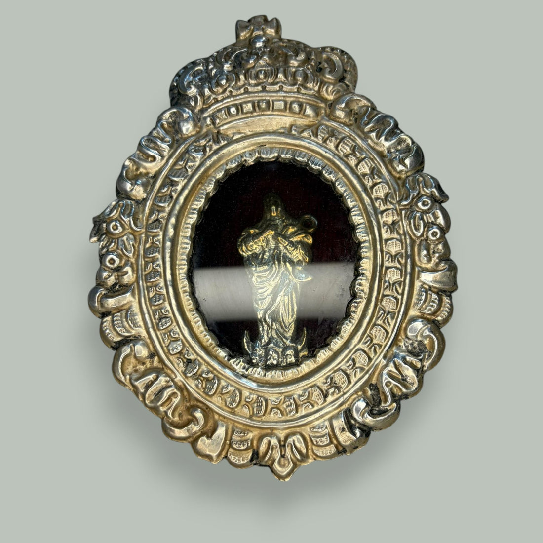 Este relicario de metal plateado con imagen de la Virgen es una pieza devocional de gran encanto, concebida originalmente para custodiar una imagen sagrada en el ámbito doméstico, acompañando la oración privada y la contemplación cotidiana. 