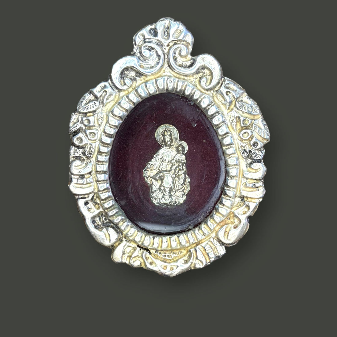 Este relicario de metal plateado con imagen de la Virgen del Carmen es una pieza devocional de pequeño formato, concebida originalmente para custodiar una imagen sagrada y acompañar la oración privada en el ámbito doméstico. 