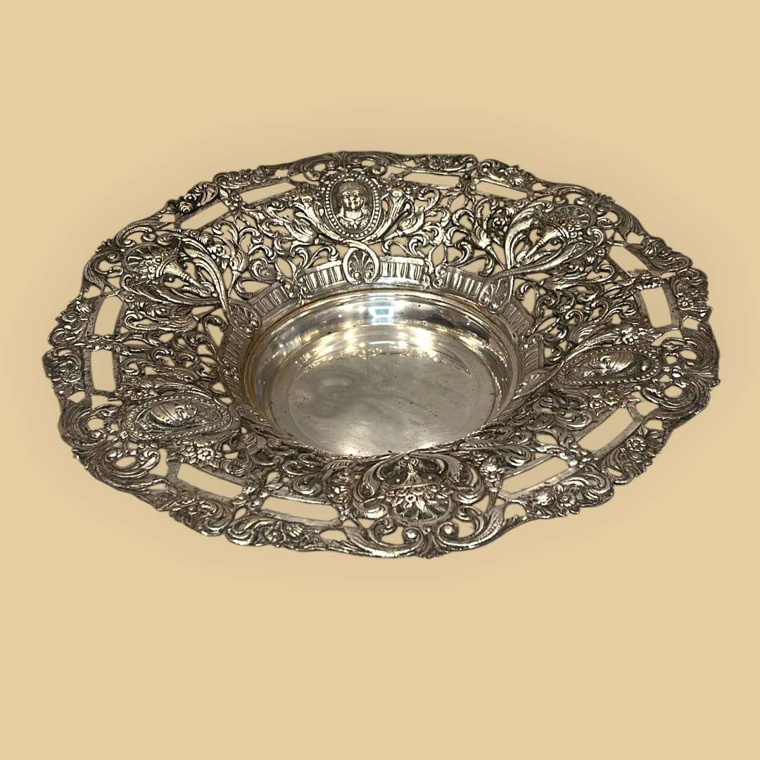 Este plato de metal plateado es una pieza decorativa de gran atractivo visual, creada para realzar la mesa, el aparador o una vitrina con un lenguaje ornamental rico y elegante. 