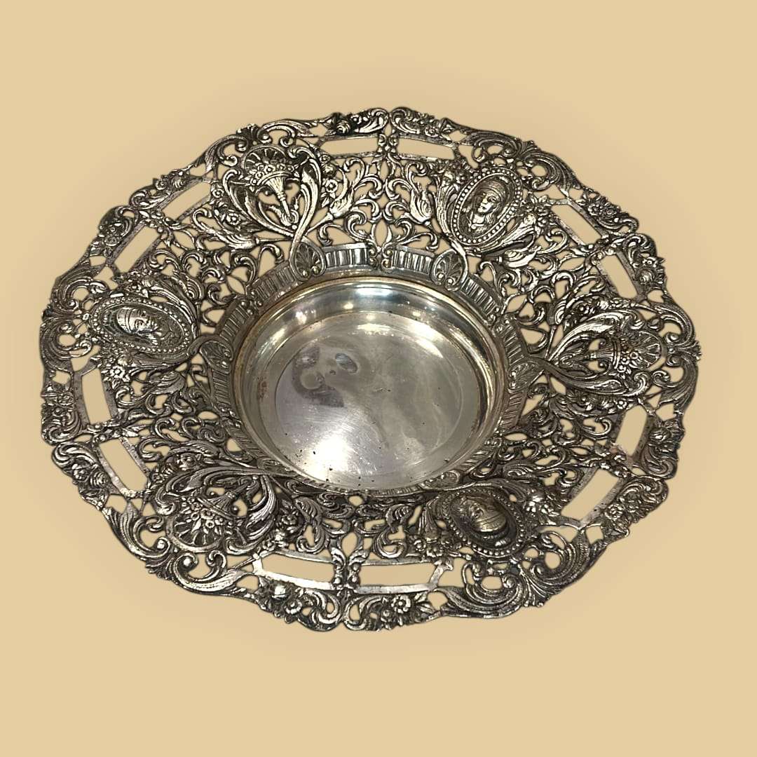 Este plato de metal plateado es una pieza decorativa de gran atractivo visual, creada para realzar la mesa, el aparador o una vitrina con un lenguaje ornamental rico y elegante. 