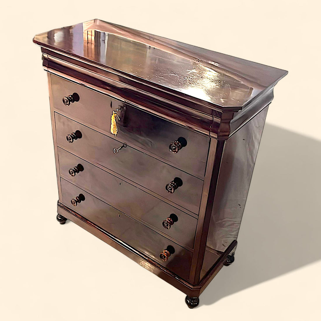 Cómoda antigua de caoba en perspectiva lateral izquierda, mostrando la amplitud de la tapa superior y la veta natural de la madera en el costado.