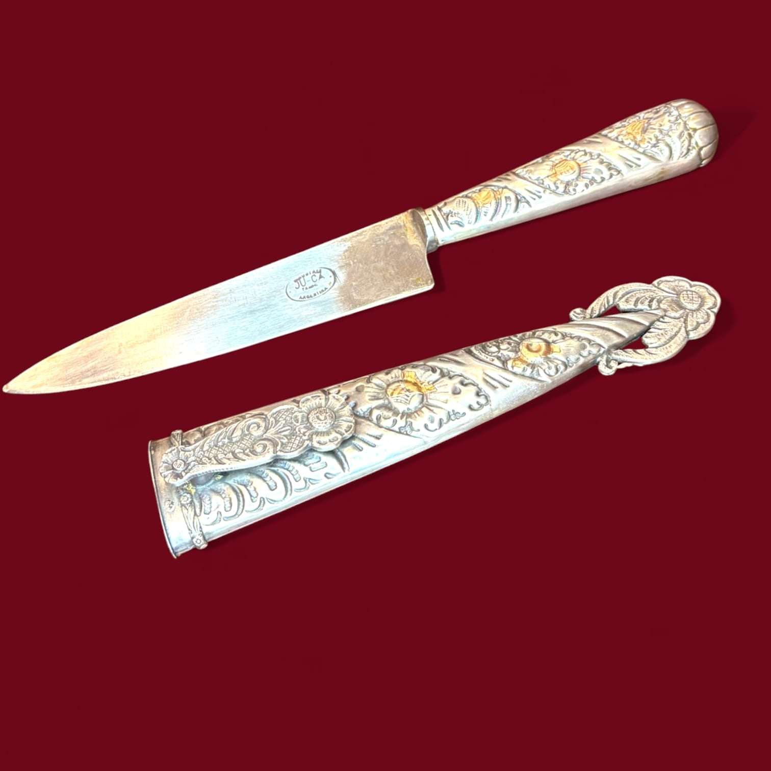 Pieza antigua de carácter decorativo y de colección, compuesta por daga y funda a juego en metal plateado. Presenta una estética muy ornamental, con abundantes relieves y una composición visual especialmente cuidada. 