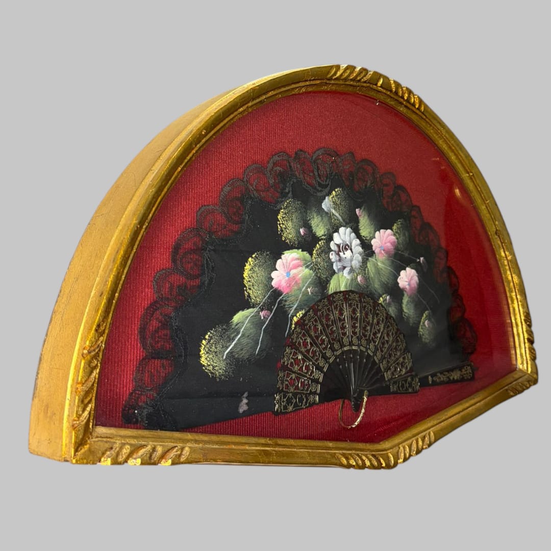 En su interior, esta Abaniquera alberga un abanico negro decorativo, con delicados motivos florales en tonos suaves que contrastan de forma elegante sobre el fondo oscuro. 