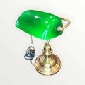  Su pantalla curva en tono verde intenso, combinada con una base metálica dorada de perfil torneado, crea una pieza con alma vintage, ideal para despachos, bibliotecas, estudios, recepciones o rincones de lectura. La silueta recuerda al universo de las lámparas de banquero, muy apreciadas en decoración por su elegancia sobria y