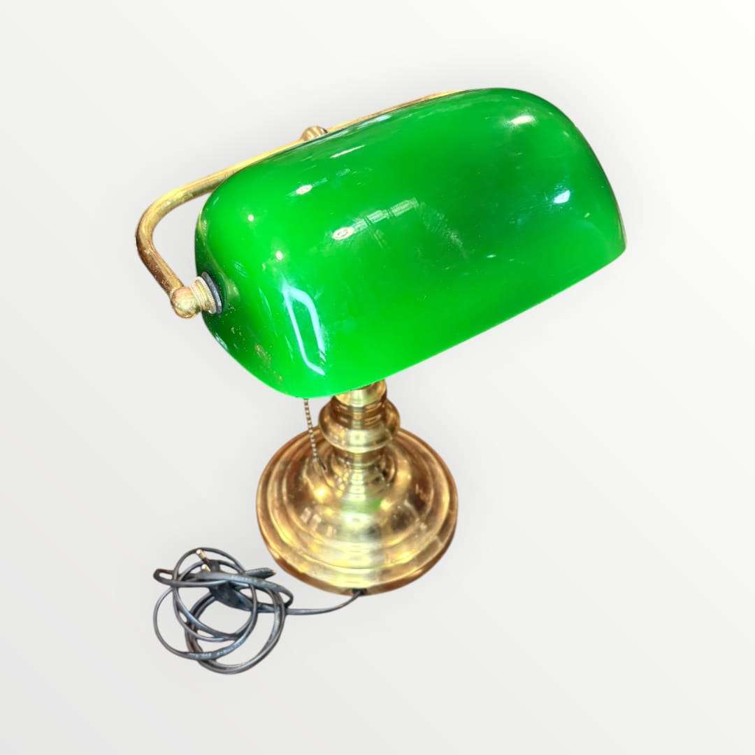  Su pantalla curva en tono verde intenso, combinada con una base metálica dorada de perfil torneado, crea una pieza con alma vintage, ideal para despachos, bibliotecas, estudios, recepciones o rincones de lectura. La silueta recuerda al universo de las lámparas de banquero, muy apreciadas en decoración por su elegancia sobria y