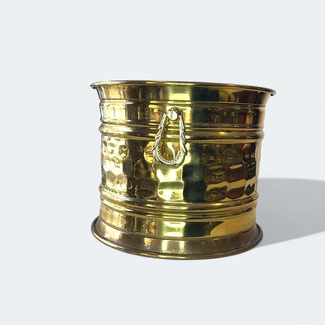 En las imágenes se aprecia un diseño sobrio y elegante, con estructura cilíndrica de líneas limpias, boca ligeramente acampanada, base ancha y estable, y un cuerpo enriquecido por un martelé irregular que multiplica los reflejos de la luz.