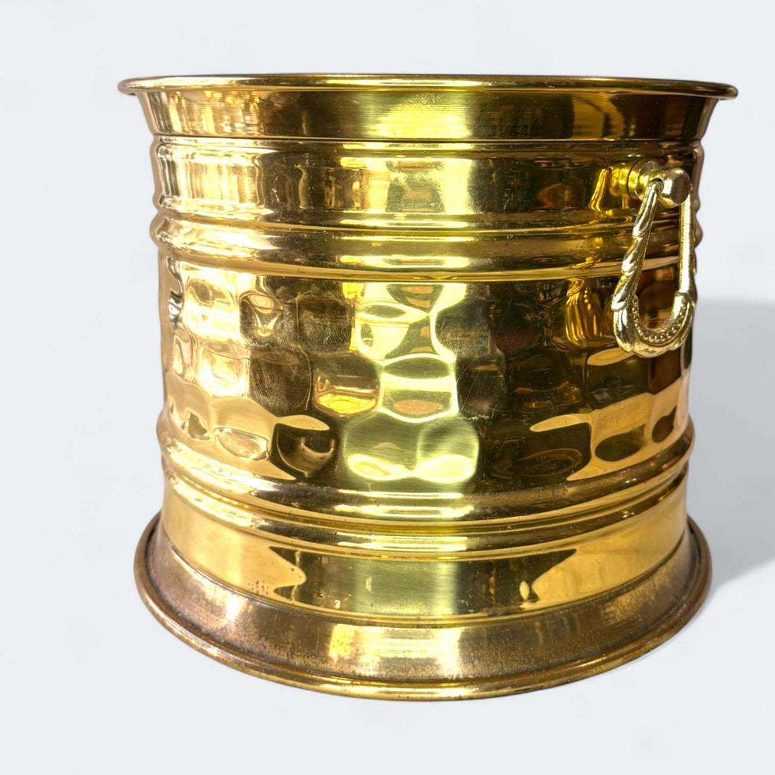 En las imágenes se aprecia un diseño sobrio y elegante, con estructura cilíndrica de líneas limpias, boca ligeramente acampanada, base ancha y estable, y un cuerpo enriquecido por un martelé irregular que multiplica los reflejos de la luz.