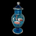 Este elegante Tibor de cristal azul es una pieza decorativa que destaca por su belleza exótica y su delicado trabajo artesanal. 